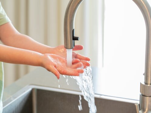 A suburban home in Texas with running warm water and a set of hands in the sink.