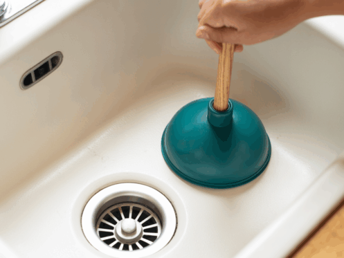 Close-up of a kitchen sink with a plunger, illustrating a DIY unclogging method.