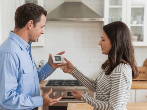 Technician explaining thermostat settings to a homeowner in a modern kitchen.