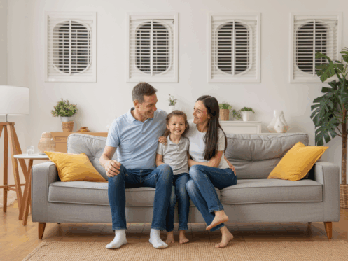 Family relaxing in a living room with visible air vents, indicating clean air from a maintained HVAC system.