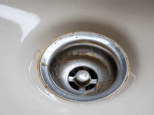 Close-up view of a bathroom sink drain clogged with hair and soap scum.