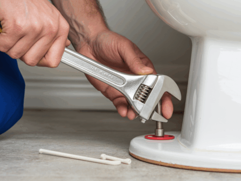 Hands using a wrench to replace a toilet wax ring.