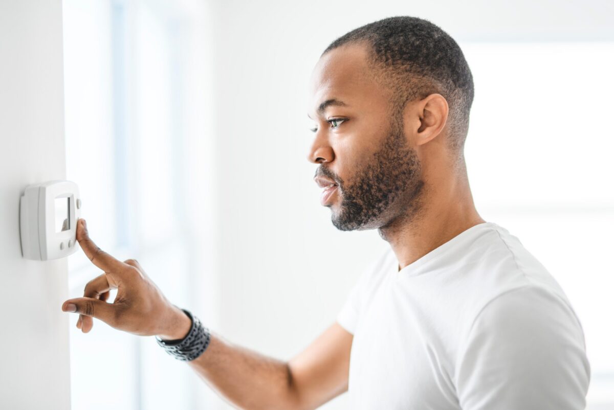 A man pushing the button on a modern thermostat that has no power, in a cozy home setting.