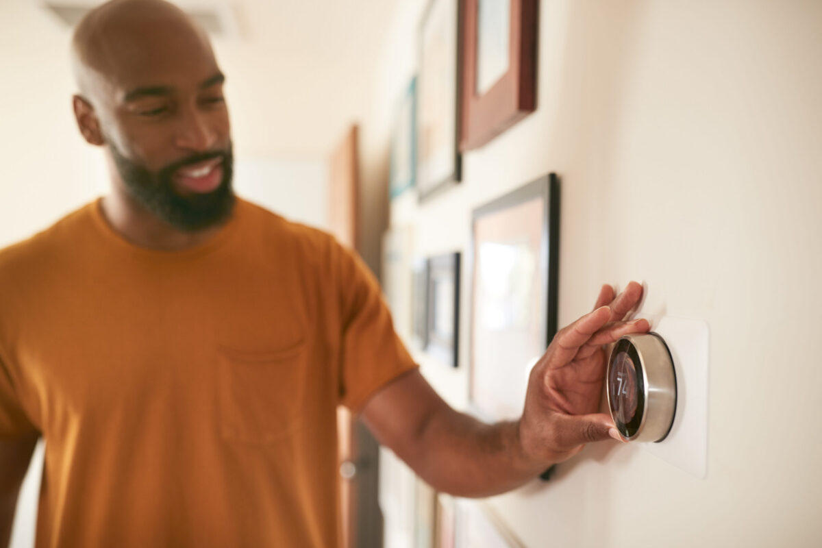 A cozy living room in a Texas home with a man turning on his heat using the thermostat.