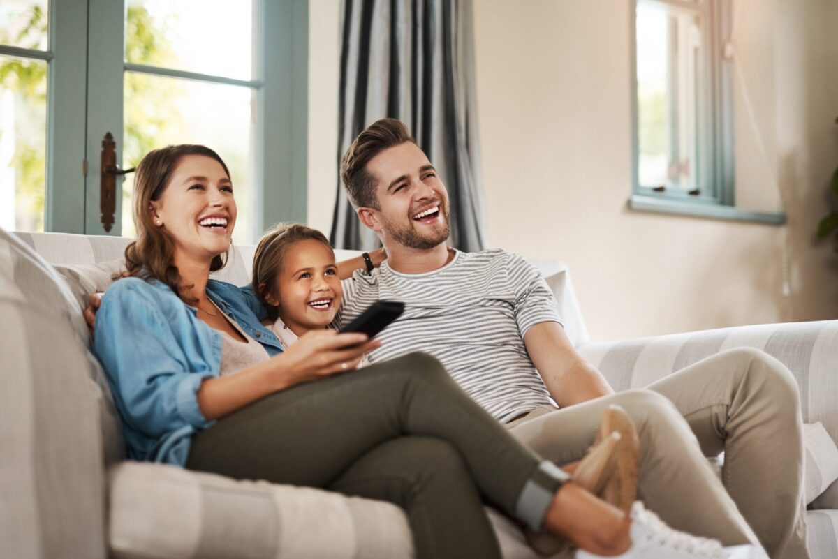 A modern home interior, with a happy family sitting on the couch after they stopped water from leaking in their AC unit.