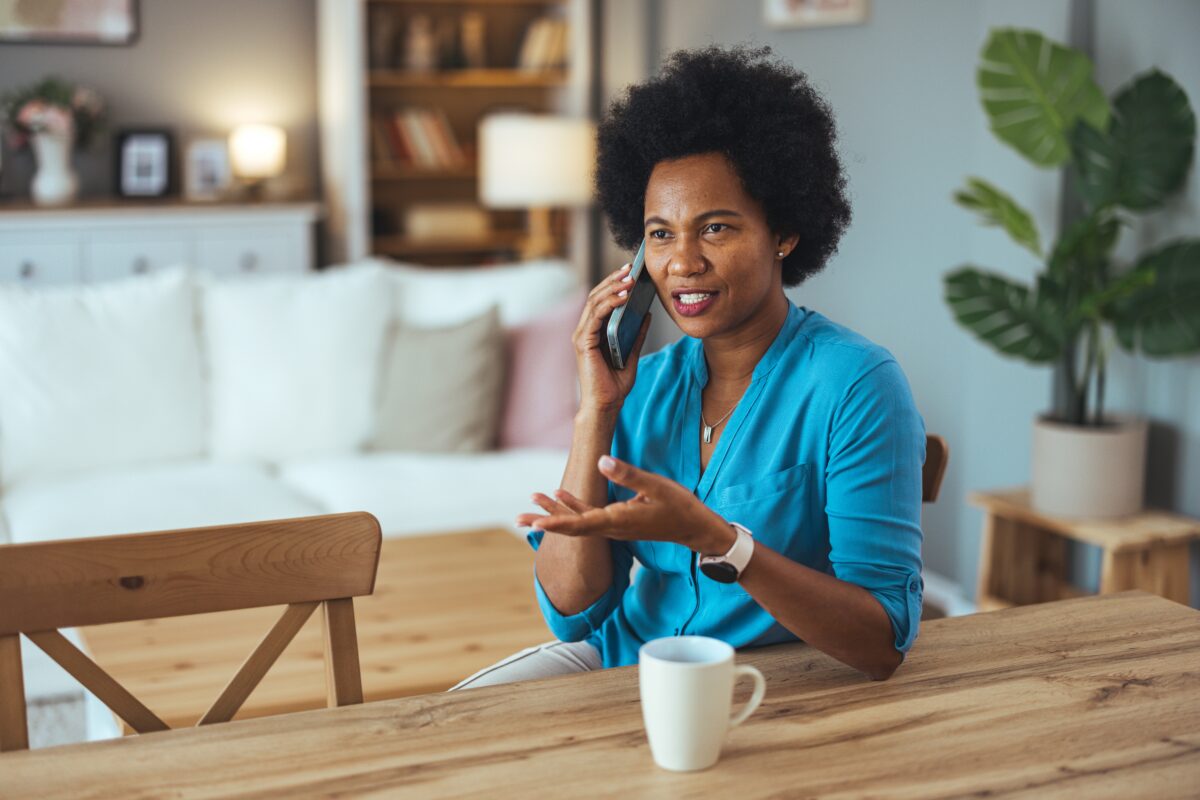 Woman on the phone with a technician asking why her furnace is making noise when it's off, while sitting at her kitchen table.