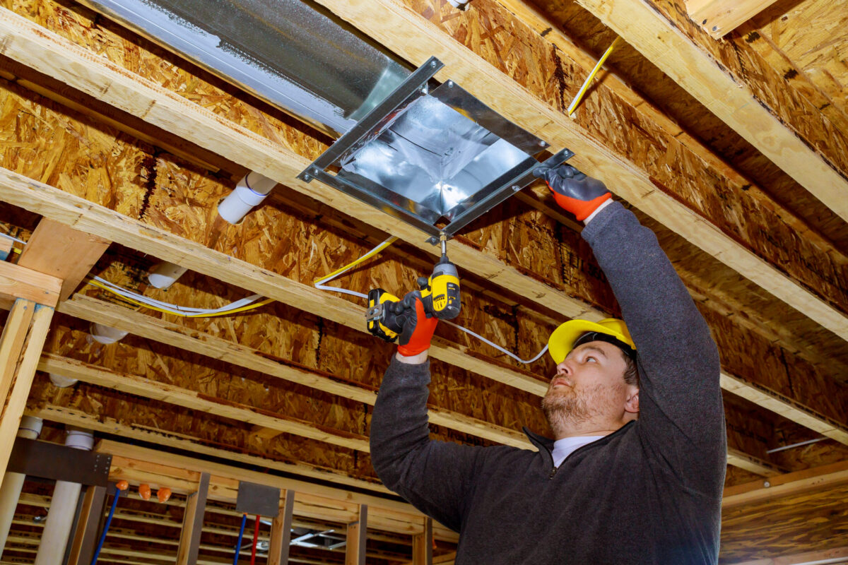 HVAC technician working on ductwork in a modern home with air conditioning and heating elements visible.