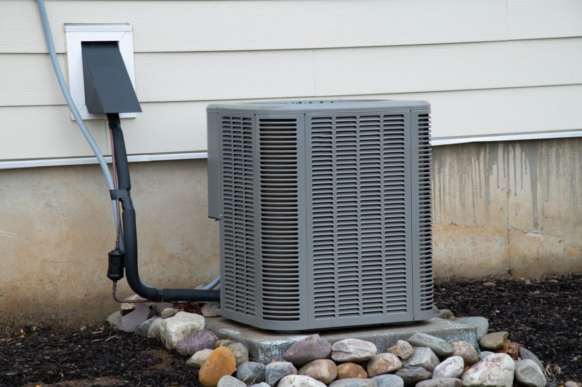 An air conditioning unit outside a cozy Texas home, surrounded by warm rocks.